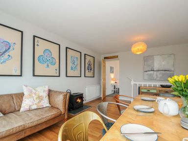 A living and dining area with a leather sofa and framed playing card artwork on the wall at Waves Edge in Looe