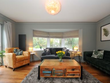 A living room with a yellow armchair gray sofa green velvet couch wooden coffee table and three windows at Waves Edge in Looe