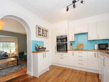 A kitchen with white cabinets wood countertops and blue backsplash next to a living room with wooden coffee table at Waves Edge in Looe