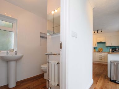 A bathroom with a pedestal sink and toilet next to a kitchen with white cabinets at Waves Edge in Looe