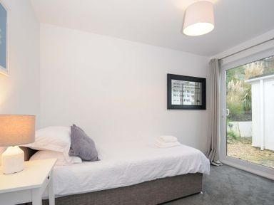 A bedroom with a single bed a bedside table with lamp a framed picture on the wall and a glass door leading outside at Waves Edge in Looe