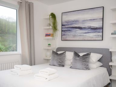 A bedroom with a bed with gray pillows and white towels on it and a painting on the wall at Waves Edge in Looe