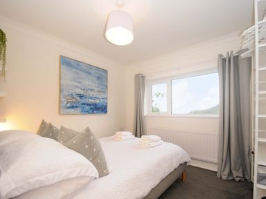 A bedroom with a double bed gray star pillows folded towels on the bed a window with gray curtains and a blue abstract painting on the wall at Waves Edge in Looe