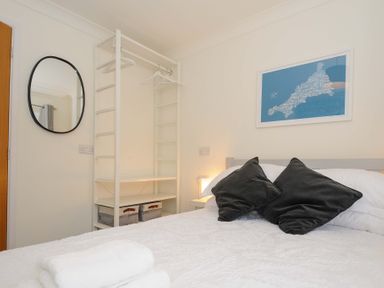 A bedroom with a bed with black pillows a white open wardrobe a round mirror and a map artwork on the wall at Waves Edge in Looe
