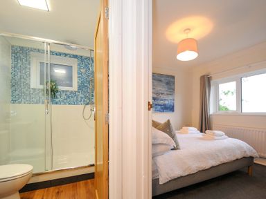 A bathroom with a shower next to a bedroom with a bed and folded towels at Waves Edge in Looe