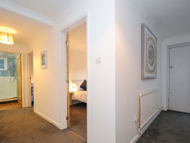 A hallway with doors leading to a bathroom and bedroom with a radiator and artwork on the walls at Waves Edge in Looe
