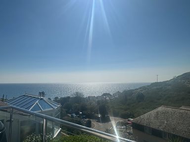 View of the ocean from a balcony with rooftops and greenery below at Waves Edge in Looe