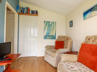 A sitting room with two armchairs a small television on a table and books above a door at Fox Cove near St Merryn