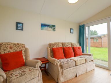 A living room with floral patterned sofas and red cushions next to a glass door at Fox Cove near St Merryn