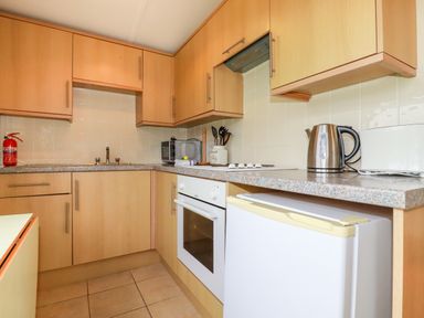 A kitchen with wooden cabinets a white oven a countertop with a kettle toaster and microwave at Fox Cove near St Merryn