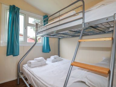 A bedroom with a metal bunk bed with folded towels on the bottom bed and blue curtains on the window at Fox Cove near St Merryn