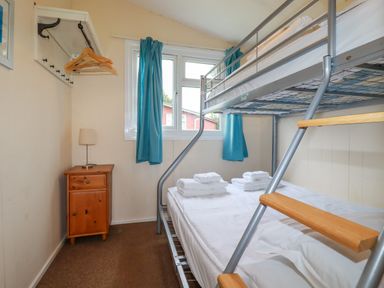 A bedroom with a bunk bed a wooden nightstand with a lamp a window with blue curtains and wall-mounted hooks with hangers at Fox Cove near St Merryn