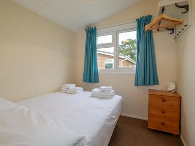 A bedroom with a bed with folded towels on it a window with blue curtains a wooden dresser and hangers at Fox Cove near St Merryn
