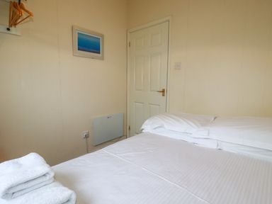 A bedroom with a bed made with white sheets folded towels on the bed a white door and a painting on the wall at Fox Cove near St Merryn