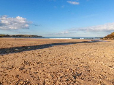 A sandy beach with a stream running to the ocean and cliffs in the distance at Fox Cove near St Merryn