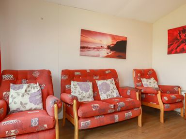 A living room with red patterned chairs and a red sunset picture on the wall at Pepper Cove near St Merryn