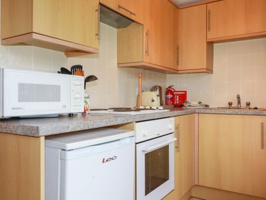 A kitchen with wooden cabinets a microwave a small refrigerator an oven a kettle a toaster and a fire extinguisher at Pepper Cove near St Merryn