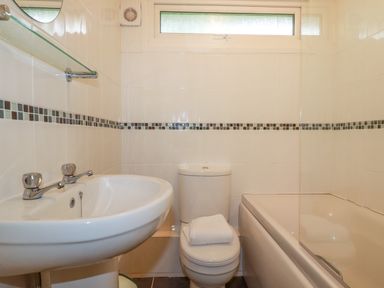 A bathroom with a sink a toilet with a towel on it and a bathtub with tiled walls at Pepper Cove near St Merryn