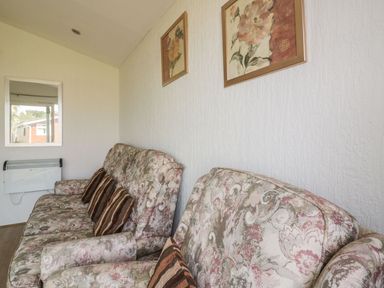 A living room with patterned sofas and cushions and framed floral wall art at Warren Cove near St Merryn