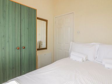 A bedroom with a bed with white linens and rolled towels near a green wardrobe and a white door at Warren Cove near St Merryn