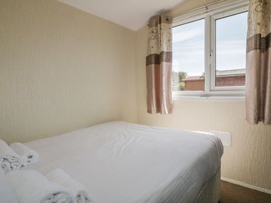 A bedroom with a bed covered in white linens and rolled towels near a window with curtains at Warren Cove near St Merryn