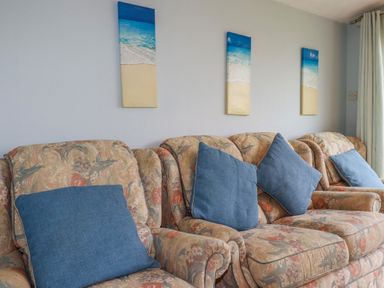 A living room with patterned sofas and blue cushions below beach-themed wall art at High Cove near St Merryn