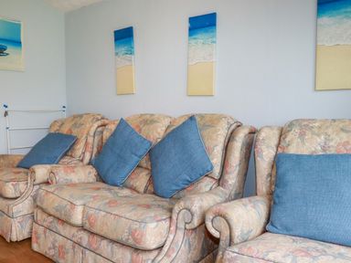 A living room with floral sofas and blue cushions under beach paintings at High Cove near St Merryn