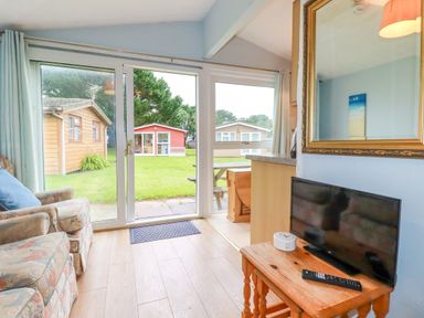 A living room with a floral armchair a wooden table with a TV and remote control glass sliding doors opening to a garden at High Cove near St Merryn