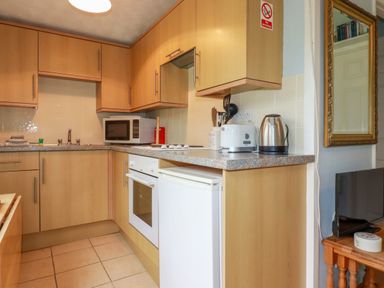 A kitchen with wooden cabinets a microwave oven toaster kettle and a small refrigerator at High Cove near St Merryn