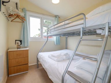 A bedroom with a bunk bed a chest of drawers with a lamp and hangers on a rack near a window at High Cove near St Merryn