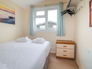 A bedroom with a bed with folded towels a window with curtains a chest of drawers and hangers on hooks at High Cove near St Merryn