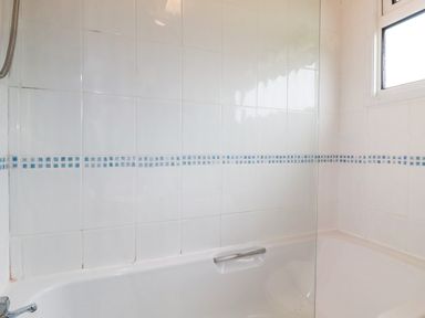 A bathroom with a white bathtub a glass shower screen and tiled walls near St Merryn