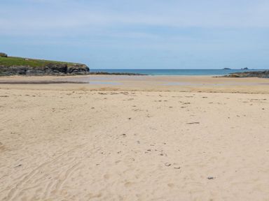A sandy beach with some rocks and grass on the left and the sea in the background at High Cove near St Merryn