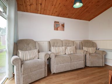 A sitting room with three beige armchairs and a beach photo on the wall at Hawkers Cove near St Merryn