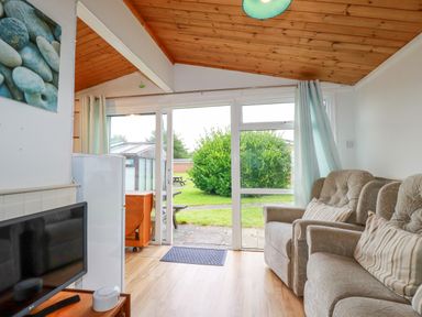 A living room with armchairs a television and glass doors opening to a garden at Hawker's Cove near St Merryn