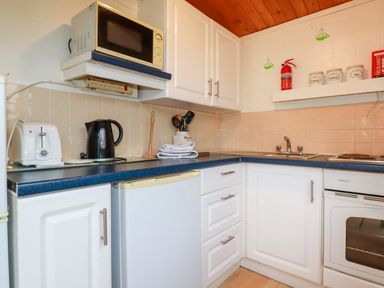 A kitchen corner with white cabinets a microwave kettle toaster sink stove and kitchen containers at Hawker's Cove near St Merryn