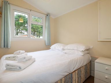 A bedroom with a bed made with white sheets and towels on it next to a window with light blue curtains at Hawkers Cove near St Merryn