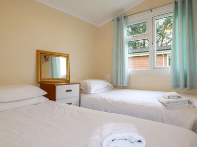 A bedroom with two single beds a dresser with a mirror and a window with blue curtains at Hawker's Cove near St Merryn
