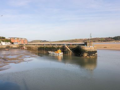 A harbor with boats docked near a stone pier with a slow speed sign at Hawker's Cove near St Merryn