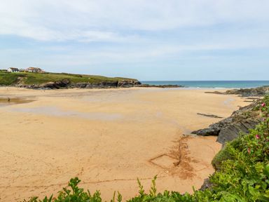 A sandy beach with rocks and grassy cliffs with houses in the distance near St Merryn