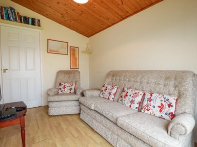 A living room with a sofa and armchair with floral cushions and wooden ceiling at Newtrain Bay near St Merryn