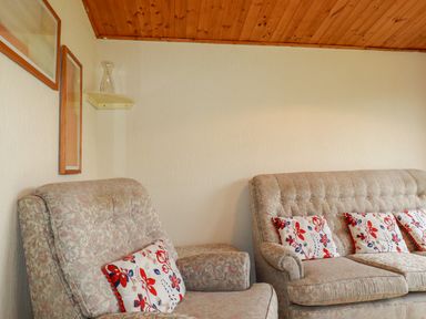 A living room with two floral armchairs a floral sofa with patterned cushions a wooden ceiling and wall shelf at Newtrain Bay near St Merryn