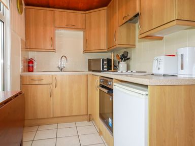 A kitchen with wooden cabinets a sink a microwave toaster and kettle at Newtrain Bay near St Merryn
