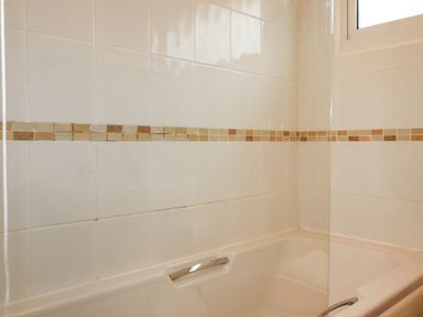 A bathroom with a beige bathtub and tiled walls with a strip of small square tiles near a window at Newtrain Bay near St Merryn
