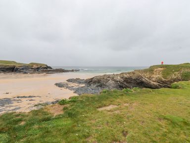 A coastal scene with a sandy beach rocks and grassy cliffs at Newtrain Bay near St Merryn