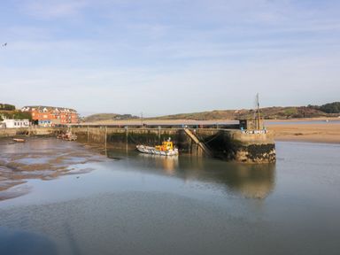 A harbor with boats docked next to a pier and buildings in the background at Newtrain Bay near St Merryn