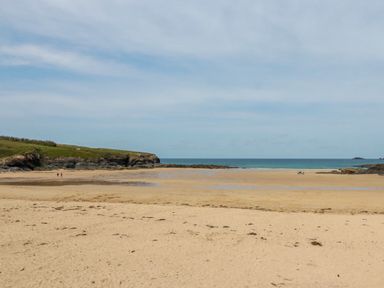A sandy beach with a grassy headland and people walking near the water at Newtrain Bay near St Merryn