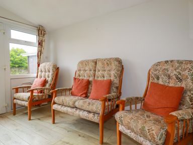 Three floral patterned armchairs with orange cushions in a room with wooden floor and white wall at Constantine Bay near St Merryn