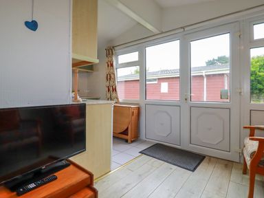 A room with a television on a wooden stand a door with windows and a chair near Constantine Bay near St Merryn