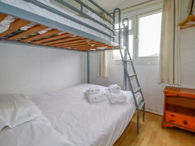 A bunk bed with folded towels on the bottom bed next to a wooden nightstand and a window in a small bedroom at Constantine Bay near St Merryn